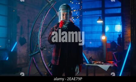 Young Beautiful Empowering Woman with Ear Piercing Wear Safety Mask and Gently Smiles at the Camera. Authentic Fabricator Wearing Work Clothes in a Stock Photo