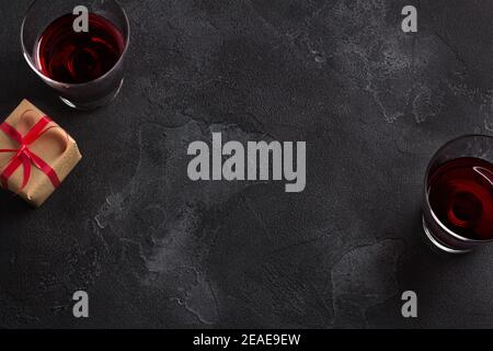 Black background with two glasses of red wine and a gift in craft paper with a red ribbon, top view, copy space Stock Photo