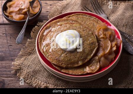 Vegetarian buckwheat pancakes with baked apples with cinnamon, honey and fresh cream on a wooden table, rustic style, horizontal. delicious healthy fo Stock Photo