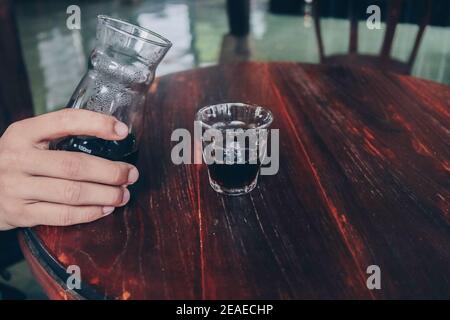 Hand pouring of v60 black coffee from unique beaker coffee glass jar on the wooden table. Stock Photo