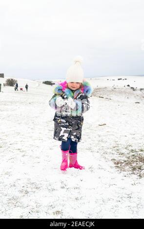 Brighton UK 9th February 2021 - Four year old Isabella enjoys making snowballs in the snow at Devils Dyke on the South Downs Way just north of Brighton today as some parts of Britain experience the coldest day of winter so far : Credit Simon Dack / Alamy Live News Stock Photo