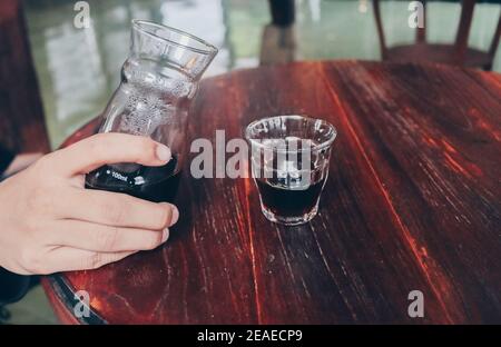 Hand pouring of v60 black coffee from unique beaker coffee glass jar on the wooden table. Stock Photo