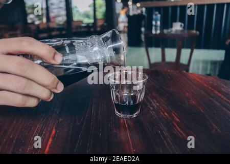 Hand pouring of v60 black coffee from unique beaker coffee glass jar on the wooden table. Stock Photo