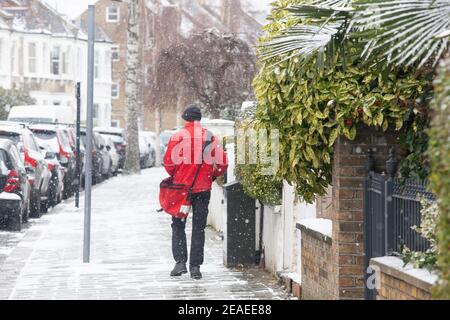 London, UK. 9 February 2021: After three days of snow in London it is starting to settle and winds have dropped as Storm Darcy has passed. In Clapham postman in a red coat delivers mail as normal. Anna Watson/Alamy Live News Stock Photo