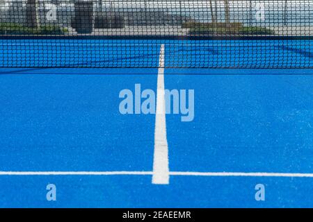Bright blue tennis, paddle ball or pickleball court ground view with white line towards black net outdoors. Stock Photo