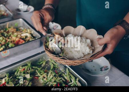 Person hand puts Chicken Yakiniku from the steel pan to wooden paper plate during lunch in restaurant Stock Photo