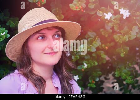 Young woman in straw hat looking at white flowers on a tree, copy space. Portrait of a woman near a flowering tree, close-up Stock Photo