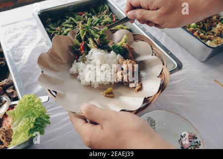 Person hand puts Chicken Yakiniku from the steel pan to wooden paper plate during lunch in restaurant Stock Photo