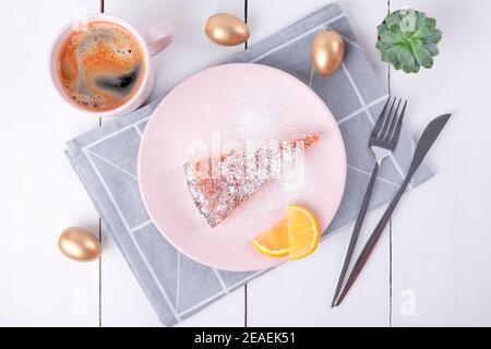 A piece of pie on a pink plate with a knife and fork on a folded linen napkin with a geometric pattern and a mug of coffee. Golden Easter eggs. Homema Stock Photo