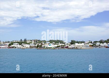 View at the waterfront, Saint George's, that is marked by pastel colored buildings with white roofs, calm blue ocean and blue sky covered with clouds. Stock Photo