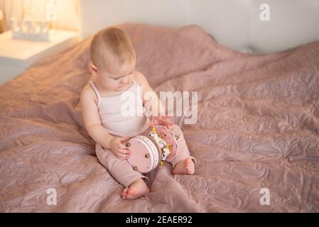 Cute baby girl playing with wooden toys at home bedroom. Modern nursery interior in pink color Stock Photo