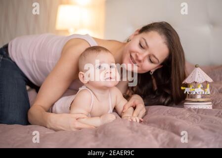 Young beautiful mother with her baby daughter playing with handmade wooden toy in bedroom Stock Photo