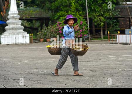 Laotian woman with carrying baskets over her shoulder returning from shopping in the green market, Luang Prabang, Laos Stock Photo