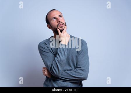 young man in studio thinking and looking toward the sky or the ceiling with thoughtful expression. pondering and imagining with hand on the chin. conc Stock Photo