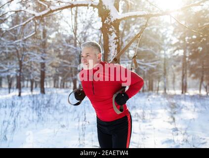 Functional training. Portrait of senior man doing exercises with fitness straps at snowy park in winter Stock Photo