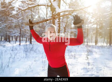 Doing endurance exercises. Senior athletic man training his arms with suspension fitness straps at snowy park Stock Photo