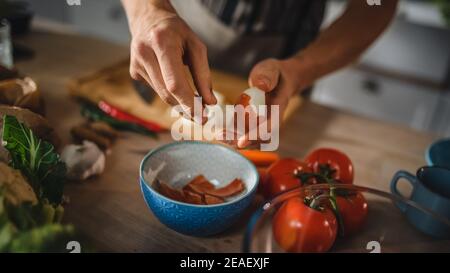 Handsome Man Peels Green Spring Onion with Hands. Man in White Shirt and Apron is Making a Organic Salad Meal in a Modern Sunny Kitchen. Natural Clean Stock Photo