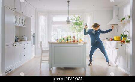 Happy Young Man with Long Hair Dancing at Home while Wearing Blue Business Suit. He is Listening to Music on a Mobile. Energetic Man Using Smartphone Stock Photo