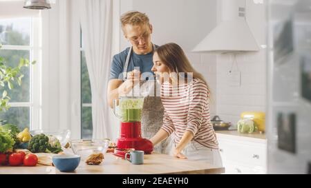 Handsome Young Man in Glasses Wearing Apron and Beautiful Girl are Making A Smoothie in the Kitchen. Happy Couple are Trying Healthy Organic Beverage Stock Photo