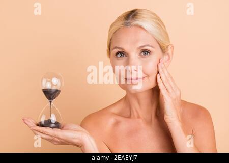 Portrait charming middle aged woman hold sand glass clock touch hands cheeks isolated pastel color background Stock Photo