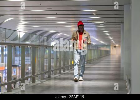 Black hipster millennial man walking in airport terminal using cellphone chatting in social networks Stock Photo