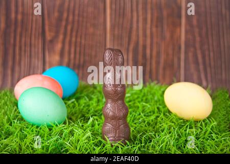 Easter chocolate bunny, colorful eggs in the grass on the wooden background. Stock Photo
