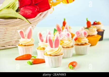 Easter funny bunny cupcake. Easter celebration festive table. Basket of flowers tulips on the background Stock Photo