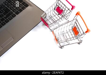 Mini shopping cart or trolley next to the laptop. Online shopping concept that enables people to shop easily and quickly. Isolated on white background Stock Photo