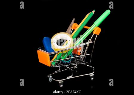 Mini shopping trolley isolated on black background. There are school items like pencil erasers in the shop cart. Shopping for school needs. Stock Photo