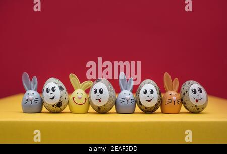 colorful cute Easter bunnies, Easter quail eggs with painted smiles and eyes stand next to each other in a row. Funny decorations for the spring holid Stock Photo