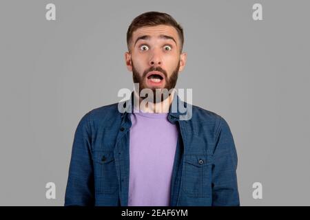 Shocked bearded guy looking at camera in panic over grey studio background Stock Photo