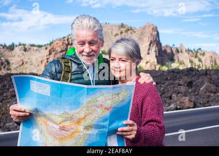 Young senior people enjoy travel and active lifestyle together - couple of old man and woman looking a map on the road - alternative retirement life a Stock Photo