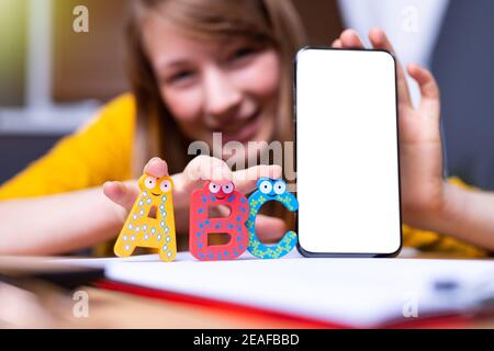 Mockup smartphone screen near ABC letters. Caucasian blonde woman smiling in background holding objects looking to the camera. Language courses, learn Stock Photo