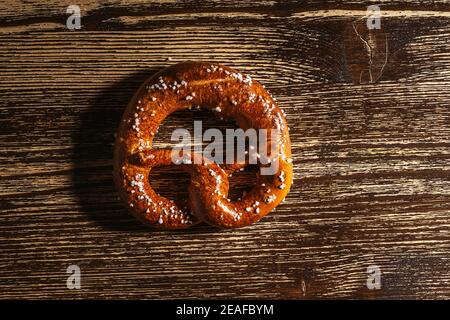 Traditional German pretzel with salt on rustic plank wood table. Bakery coffee shop, Oktoberfest card, top view, single object Stock Photo