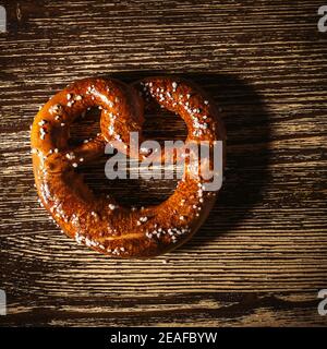 Traditional German pretzel with salt on rustic plank wood table. Bakery coffee shop, Oktoberfest card, top view, single object Stock Photo