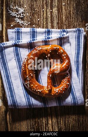 Traditional German pretzel with salt on blue white linen kitchen towel on rustic plank wood table. Bakery coffee shop, Oktoberfest card, top view, sin Stock Photo