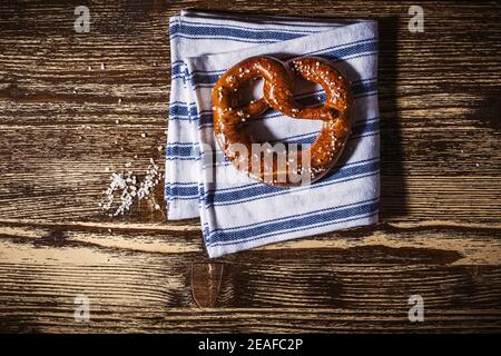 Traditional German pretzel with salt on blue white linen kitchen towel on rustic plank wood table. Bakery coffee shop, Oktoberfest card, top view, sin Stock Photo