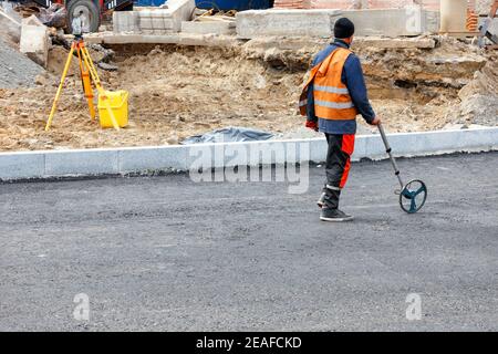 A working engineer measures road distances with a measuring wheel and determines the amount of asphalt needed to be poured on a new section of road. Stock Photo