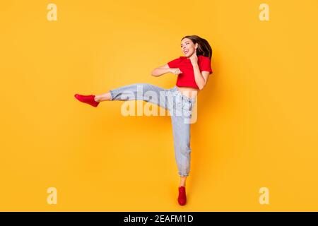 Boxer girl practicing air kicks raise leg jumping high wear red crop top jeans isolated yellow color background Stock Photo