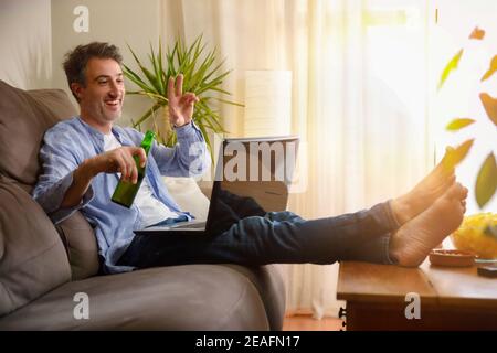 Man making video conference sitting on the sofa at home having a snack Stock Photo