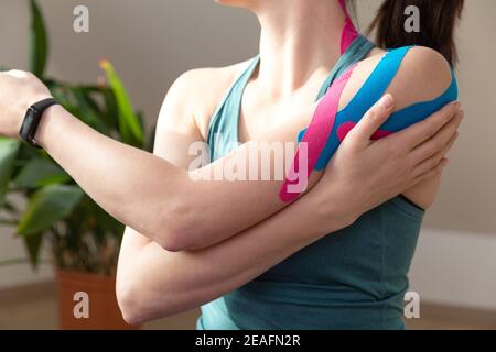 Young fit women wearing kinesio tape on her shoulder. Performing exercise at home. Kinesiology physical therapy. Stock Photo