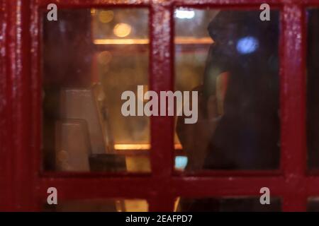 Woman on the phone in red telephone box at night. Defocused shot Stock Photo