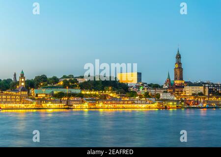 View of the Elbe riverside with the hamburger landungsbruecken building, saint michaelis church and the bismarck monument in Germany during sunset. Stock Photo