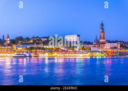 View of the Elbe riverside with the hamburger landungsbruecken building, saint michaelis church and the bismarck monument in Germany during sunset. Stock Photo