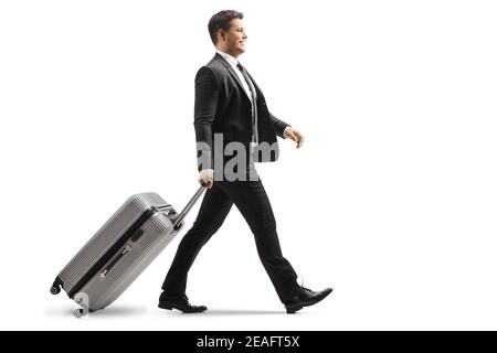 Full length profile shot of a smiling young businessman walking and pulling a suitcase isolated on white background Stock Photo