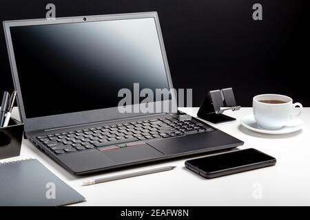 Desktop with laptop pc smart phone, notepads pens office suppliers cup of coffee drink plant flower. Home Office laptop blank template display Stock Photo