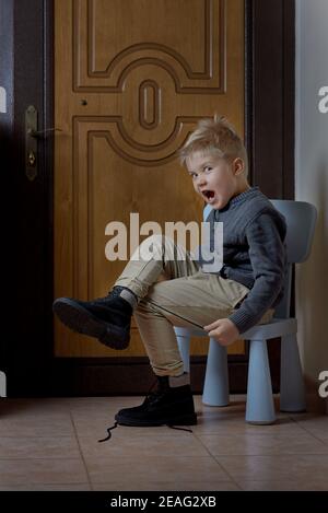 Child tying his shoes before leaving home, child looking on his boots Stock Photo
