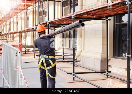 builder carries a steel beam on his shoulder. Construction site, building construction and reconstruction process. Stock Photo