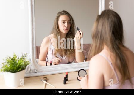 Shallow focus of a woman putting on lipstick in front of a mirror Stock Photo
