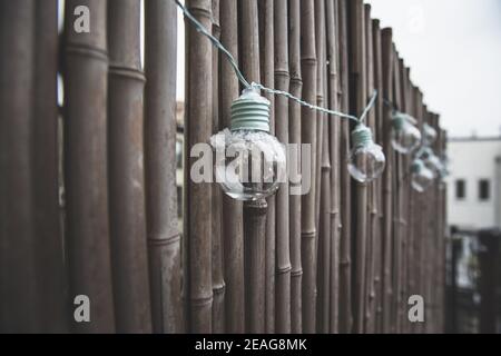 LED mint color light bulbs with wires hanging on a bamboo screen wall outside on a deck Stock Photo